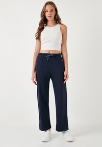 Navy zila, platu kāju bikses, kas izgatavotas no mīksta, elastīga auduma ar elastīgu jostu un mežģīni. Apvienotas ar baltu ribotu cropped topu.