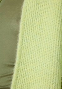 Sciarpa lavorata a maglia verde lime con trama a coste, materiale morbido e finitura leggermente soffice, posizionata accanto a una maglietta verde oliva.