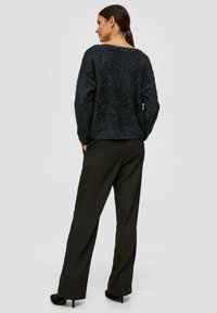 Czarny puszysty sweter z długimi rękawami, zestawiony z szerokimi czarnymi spodniami. Sweter ma teksturowane wykończenie i luźny krój.