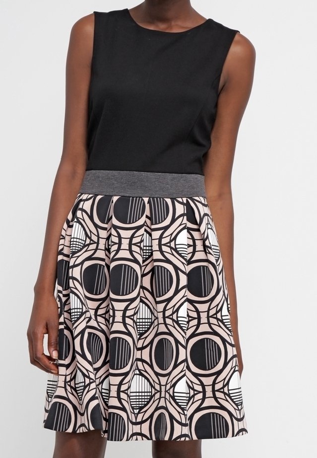 Robe sans manches noire avec une ceinture grise et une jupe plissée arborant un motif circulaire géométrique noir, blanc et rose.