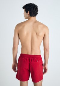 Rote Badehose mit elastischem Bund, einer einzelnen Gesäßtasche und flachem Vorderteil. Glatte Stoffoberfläche. Keine zusätzlichen Muster oder Akzente.