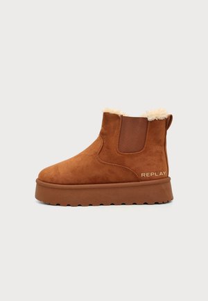 Bottine en daim marron avec semelle épaisse, panneau latéral élastique, doublure moelleuse et logo "Replay" près du talon sur fond blanc.