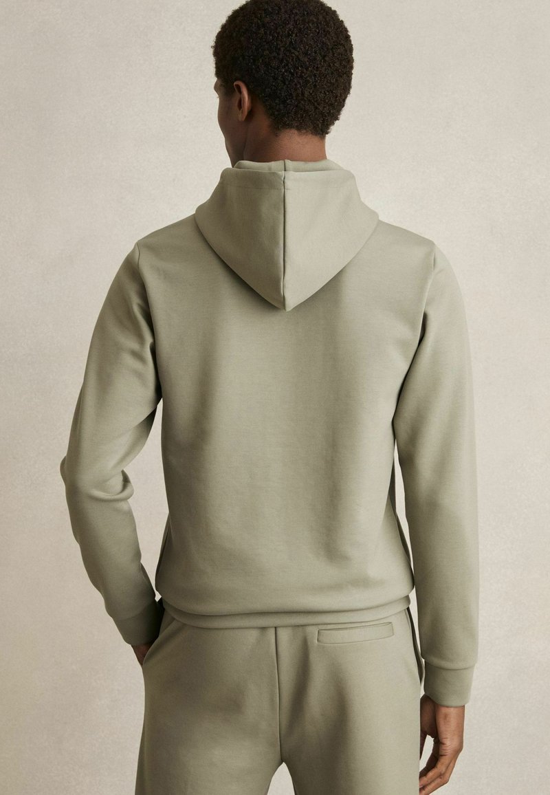 Olijfgroene hoodie, glad materiaal, slim fit ontwerp, ribbelboorden en een kangoeroezak, gecombineerd met bijpassende joggers.