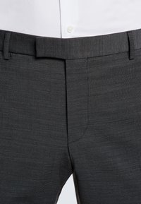 Grå skräddarsydda byxor med en fin strukturerad mönster, med platt front, bälteshällor och sidfickor, i kombination med en vit skjorta.