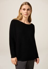 Czarny dziergany sweter z dekoltem typu łódka i długimi r�ękawami, o fakturowanym wzorze i luźnym kroju.