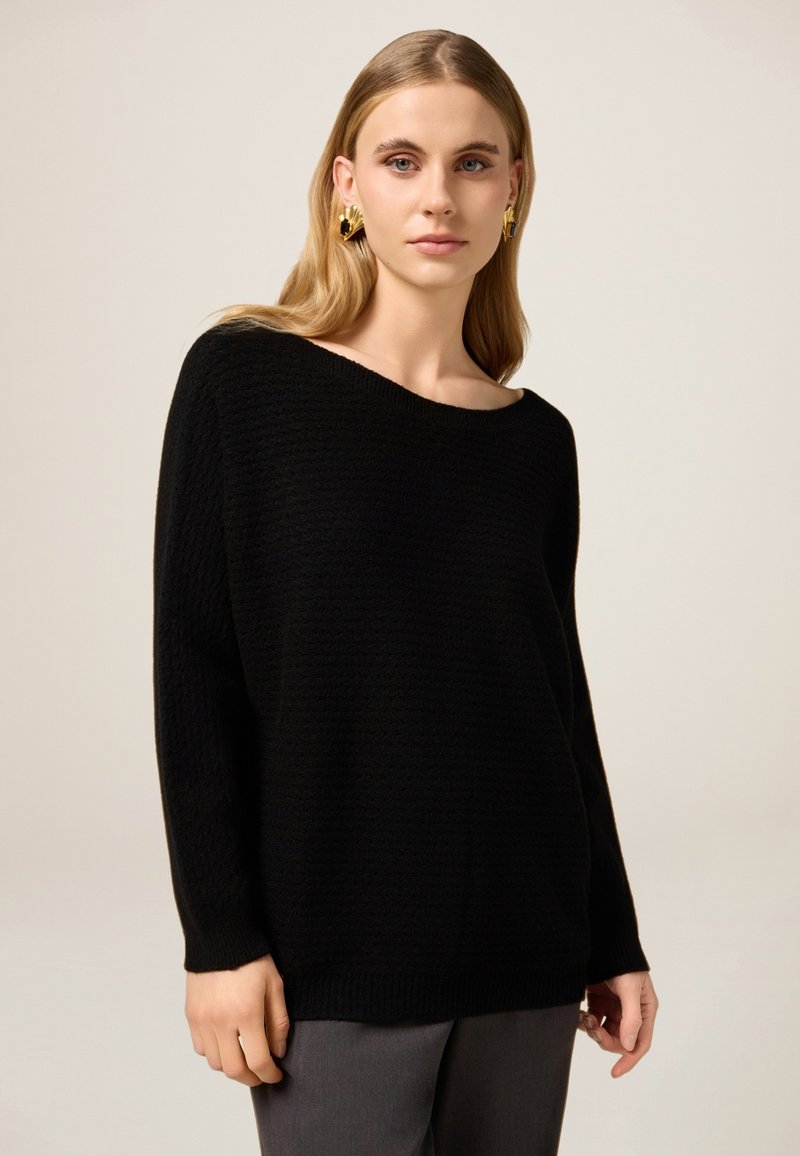 Czarny dziergany sweter z dekoltem typu łódka i długimi rękawami, o fakturowanym wzorze i luźnym kroju.
