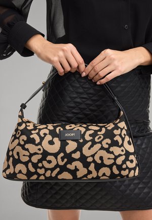 Mani che tengono una borsa leopardata nera e beige con l'etichetta "JOOP!" contro una gonna trapuntata nera e una camicetta.