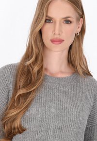 Grå strikket sweater med ribbet design, rund halsudskæring og blød tekstur, suppleret af løst, bølget hår og diskrete øreringe.