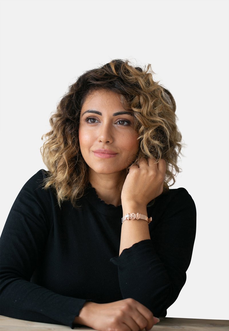 Braccialetto in oro rosa con chiusura, indossato su un polso. La persona ha i capelli ricci e lunghi fino alle spalle ed indossa una maglietta nera a maniche lunghe.