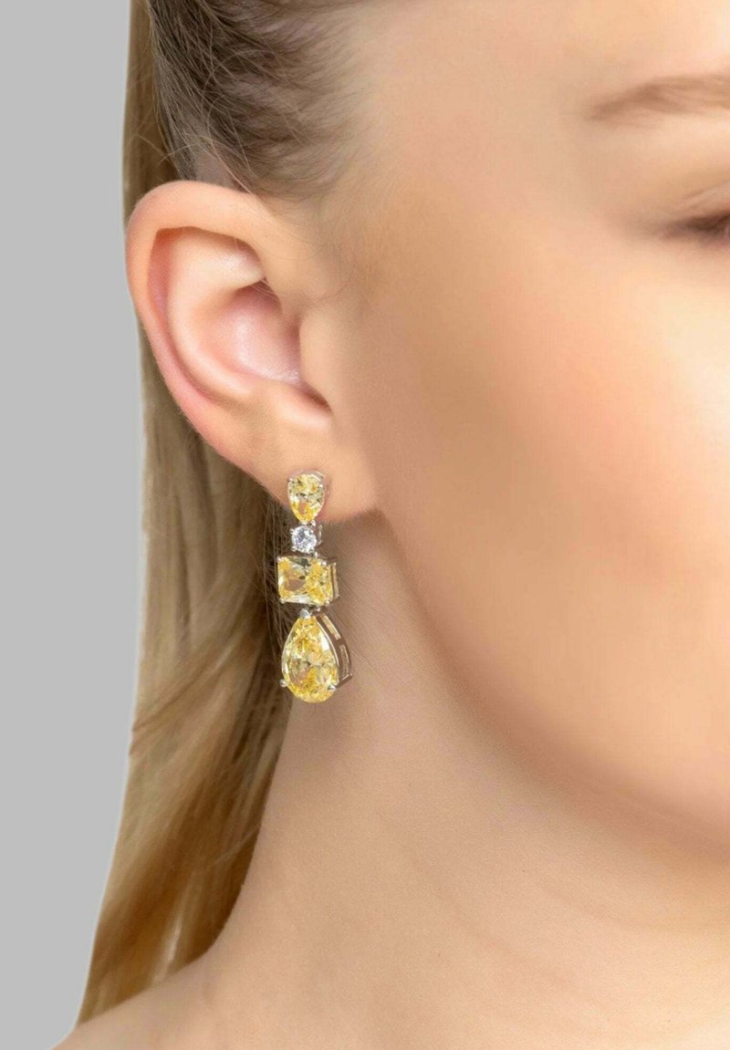 Los pendientes de gota con piedras preciosas amarillas presentan formas de pera y cuadradas, montadas en metal de tono plateado. El diseño incluye una piedra de acento transparente.