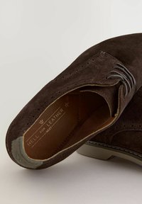 Braune Wildleder-Oxford-Schuhe mit spitz zulaufender Zehenpartie, dezenten Perforationen und kontrastierenden grauen Akzenten an der Ferse und im Innenbereich.