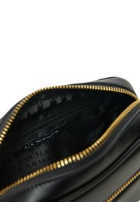 Interno di borsa in pelle nera con dettaglio della cerniera dorata. Le fodere presentano un motivo a logo ripetuto. Include una tasca interna con cerniera.