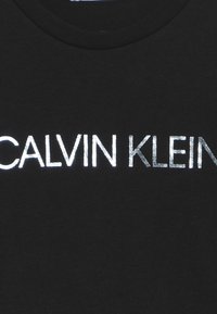Svart T-shirt i bomull med en framträdande silverlogotyp av "CALVIN KLEIN" tryckt i ett rent, modernt typsnitt centrerat på bröstet.