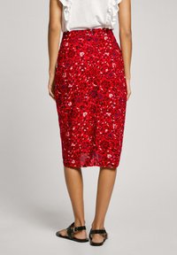 Roter Midirock mit floralem Muster in einer figurbetonten Silhouette, der mit einem lebhaften Muster aus Blumen und Blättern sowie einem glatten, leichten Stoff ausgestattet ist.