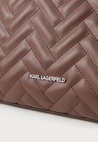 Hnedá prešívaná kožená povrchová úprava s diagonálnym prešívaním a malou striebornou tabuľkou s logom "KARL LAGERFELD".