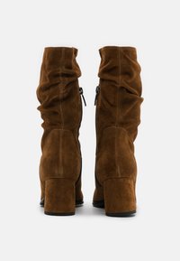 Pair of brown suede mid-calf boots with block heels, slouchy design, and visible side zippers viewed from the back on a white background.