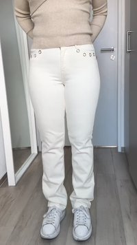 Los jeans blancos de corte recto presentan detalles metálicos en la cintura. Combinados con zapatillas blancas, en un entorno minimalista en interiores.