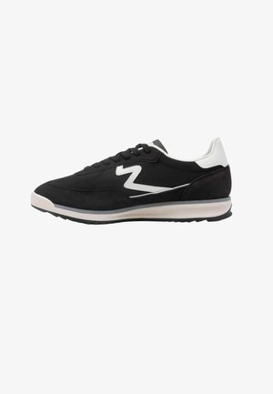 Baskets en daim noir avec des accents blancs, présentant un design en zigzag distinct, une fermeture à lacets, un col rembourré et une semelle extérieure en caoutchouc.