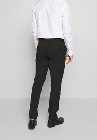 Svarta byxor med slim fit, med bakfickor med knappstängning, bärs med en vit skjorta och polerade svarta skor.