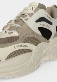 Μπεζ και λευκά αθλητικά παπούτσια Armani Exchange με πάνελ από δίχτυ και δέρμα, λευκά κορδόνια και χοντρή υφασμάτινη σόλα.
