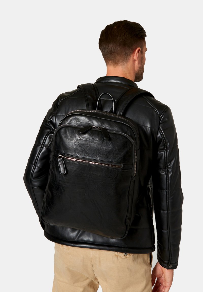 Mochila de cuero negro con una textura suave, que cuenta con un bolsillo delantero con cremallera y correas dobles para los hombros, de forma bien estructurada y rectangular.