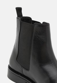 Μαύρη δερμάτινη μπότες Chelsea με λείο φινίρισμα, ελαστικές πλαϊνές πάνελ, θηλιά για εύκολη φόρεση και χαμηλό τακούνι. Καλά καθορισμένες ραφές σε όλη την επιφάνεια.