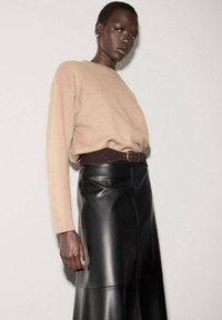 Mujer de piel oscura que lleva un suéter beige metido dentro de una falda de cuero negra de cintura alta, con un cinturón ancho marrón.