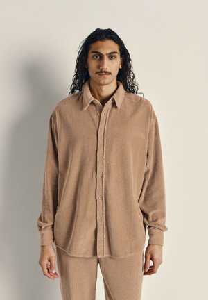 Corduroy shirt in muted beige with a button-up front, long sleeves, and a collared neck, featuring ribbed texture and a relaxed fit.