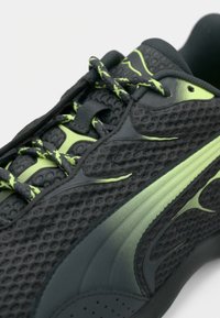 Chaussure de sport noire avec une tige texturée, des accents verts et des lacets à motifs. Présente un design élégant et une structure de soutien.