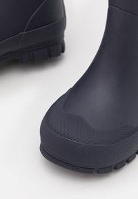 Stivale di gomma navy con superficie testurizzata, punta rotonda e suola rigata. Presenta un design senza cuciture e una costruzione robusta per la durata.