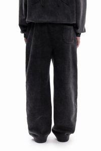 Czarne spodnie dresowe z weluru o luźnym kroju, z boczną kieszenią i fakturowanym wykończeniem. Model ma miękką, gładką powierzchnię.