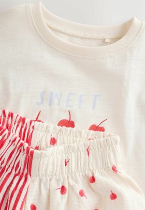 Kreemjas puuvillast särk tekstiga "SWEET" helerohelises toonis ja punase kirsi trükiga; sobivad püksid punaste triipude ja täpilise mustriga. Pehme, tekstuuriga kangas.