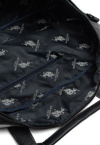Vnitřek černého batohu s texturovanou tmavě modrou podšívkou s opakujícím se vzorem loga a kapsou se zipem pro ukládání.