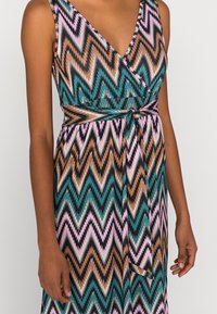 Robe à motif zigzag multicolore, avec un décolleté en V profond, sans manches, ceinture à la taille et une silhouette fluide.