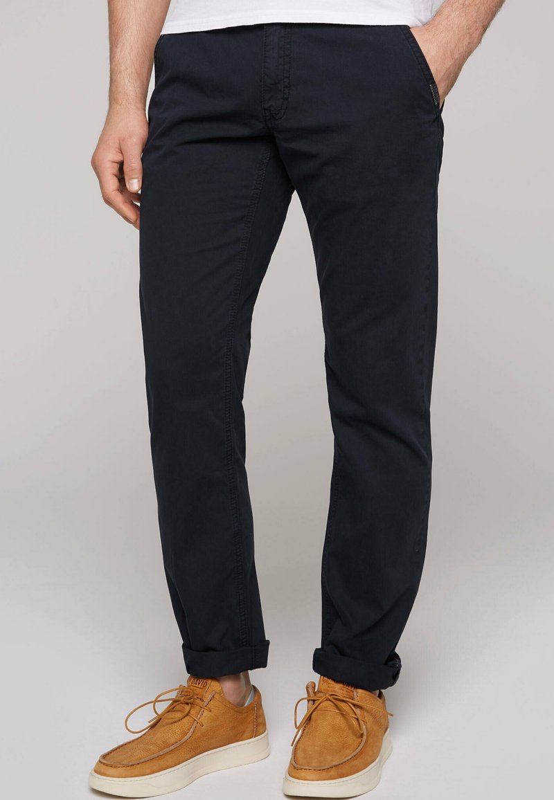 Pantaloni di cotone blu navy con taglio dritto, dotati di tasche laterali e orli arrotolati, abbinati a scarpe di pelle marrone chiaro.