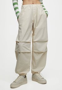 Beige Cargo-Hosen mit lockerer Passform, gerafftem Saum und elastischem Bund. Kombiniert mit off-white Sneakers mit glatter Textur.