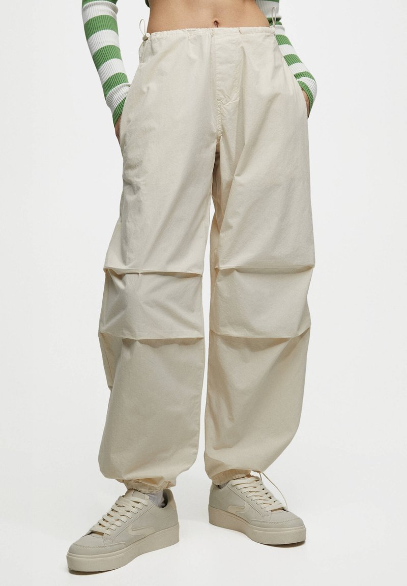 Beige Cargo-Hosen mit lockerer Passform, gerafftem Saum und elastischem Bund. Kombiniert mit off-white Sneakers mit glatter Textur.