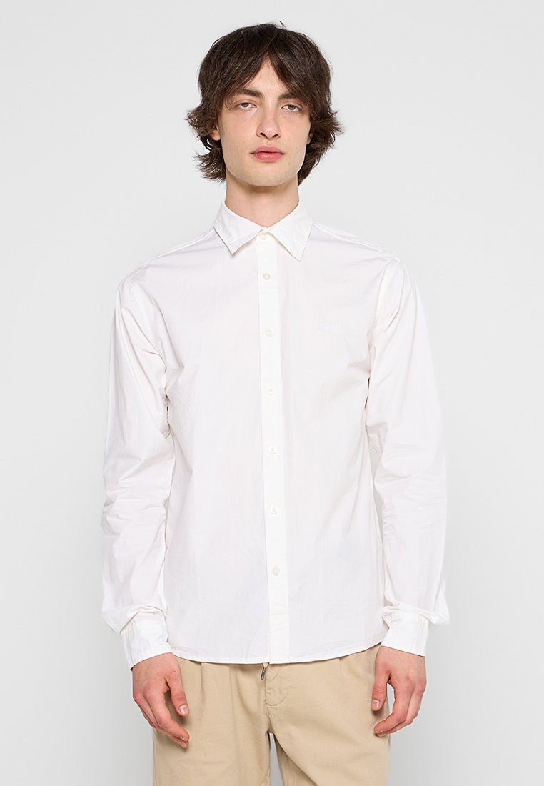 Witte lange mouwen blouse met een standaardkraag, een gladde textuur en een subtiele logo op de borst, gecombineerd met lichtbeige broek.