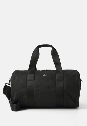 Sac polochon noir avec double poignée et bandoulière réglable, avec un petit logo crocodile argenté au centre avant.