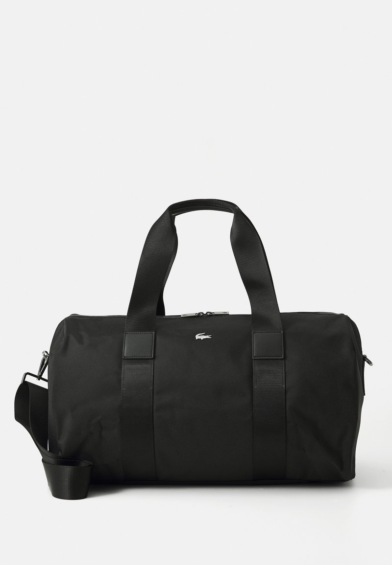 Sac polochon noir avec double poignée et bandoulière réglable, avec un petit logo crocodile argenté au centre avant.