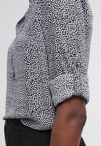 Zwart-wit gestreepte lange mouw shirt met opgerolde mouwen, gedragen met zwarte broek, zijaanzicht van arm en romp.