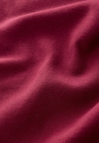 Bordowy materiał o gładkiej, delikatnej strukturze dzianiny, ukazujący łagodne fale i miękkie zagięcia, tworzący subtelną głębię w wyglądzie materiału.
