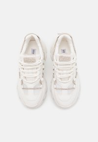 Bílé masivní tenisky s síťovinovými panely, tlustou podrážkou a ozdobami z rhinestone na tkaničkách a jazyků, zobrazené z pohledu shora na bílém pozadí.