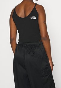 Top corto negro sin mangas con tirantes finos y un logo blanco, combinado con pantalones cargo negros con cintura elástica y bolsillos.