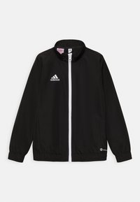 Chaqueta deportiva negra de tela lisa, con cremallera y logo blancos, mangas largas con puños elásticos y dos bolsillos laterales.
