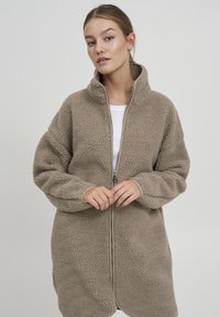 Beige fleece jasje met een hoge kraag, rits aan de voorkant en oversized mouwen. Zachte textuur met een effen kleur ontwerp.