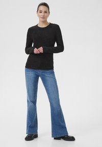 Sort langærmet top med tekstureret stof, rund halsudskæring, kombineret med lyseblå flared jeans og sorte sko. Enkel og moderne design.