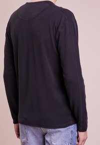Long-sleeve shirt made of dark blue cotton, with a ribbed texture, crew neckline, and contrasting stitching on the shoulders and hem.