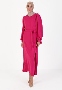 Fuchsia long-sleeve dress made of soft fabric, featuring puffed sleeves, a waist-tie belt, and a straight cut. Paired with nude high heels.