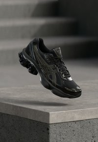 Black athletic shoe with mesh and synthetic materials, featuring a cushioned sole, lacing system, and distinctive logo accents.